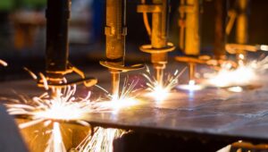 Industrial cutting heads working on a steel plate, with sparks along the cuts.